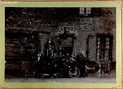 Une photographie originale ancienne en noir et blanc, d'un groupe de 12 personnes (9 hommes et 3 femmes), devant une entre de maison prenant la pose, avec quelques bouteilles en main. Un homme affal dans une charrette.